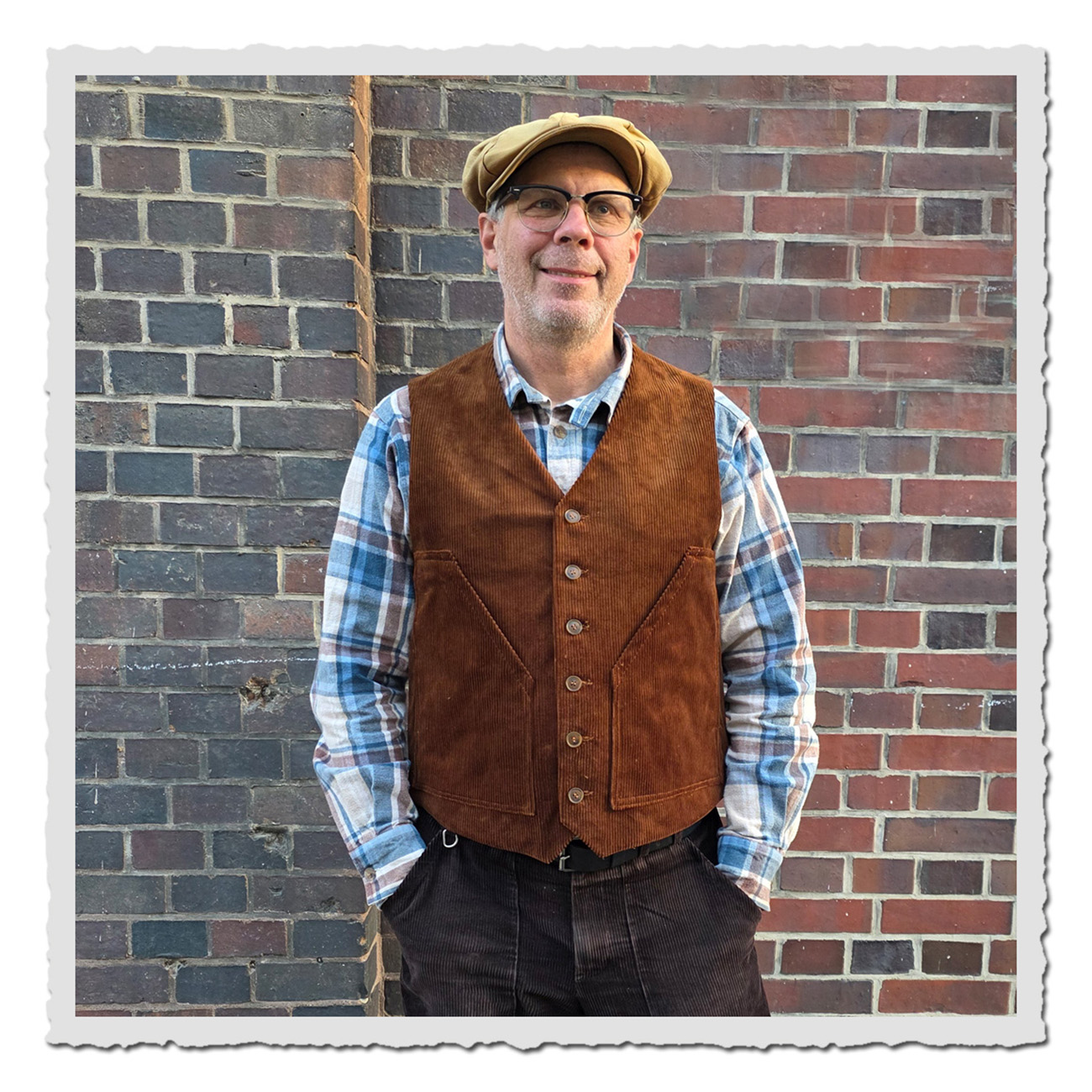 Mann vor Ziegelmauer Trägt die Erwin Weste von Retronia – traditionelle Herrenweste in Braun